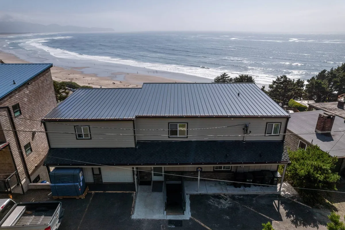 This exterior image features a serene view of the home with the breathtaking Pacific Ocean serving as a dramatic backdrop. The beach is visible, inviting guests to imagine early morning walks or relaxing by the water's edge. The house structure is prominent, situated to maximize the panoramic ocean views that define the experience at Vista House Unit B.
