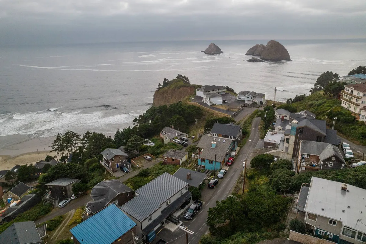 A tranquil exterior view featuring dramatic ocean waves, rock formations, a sandy beach, and coastal houses nestled along the shoreline. The image captures the expanse and beauty of the surrounding landscape.