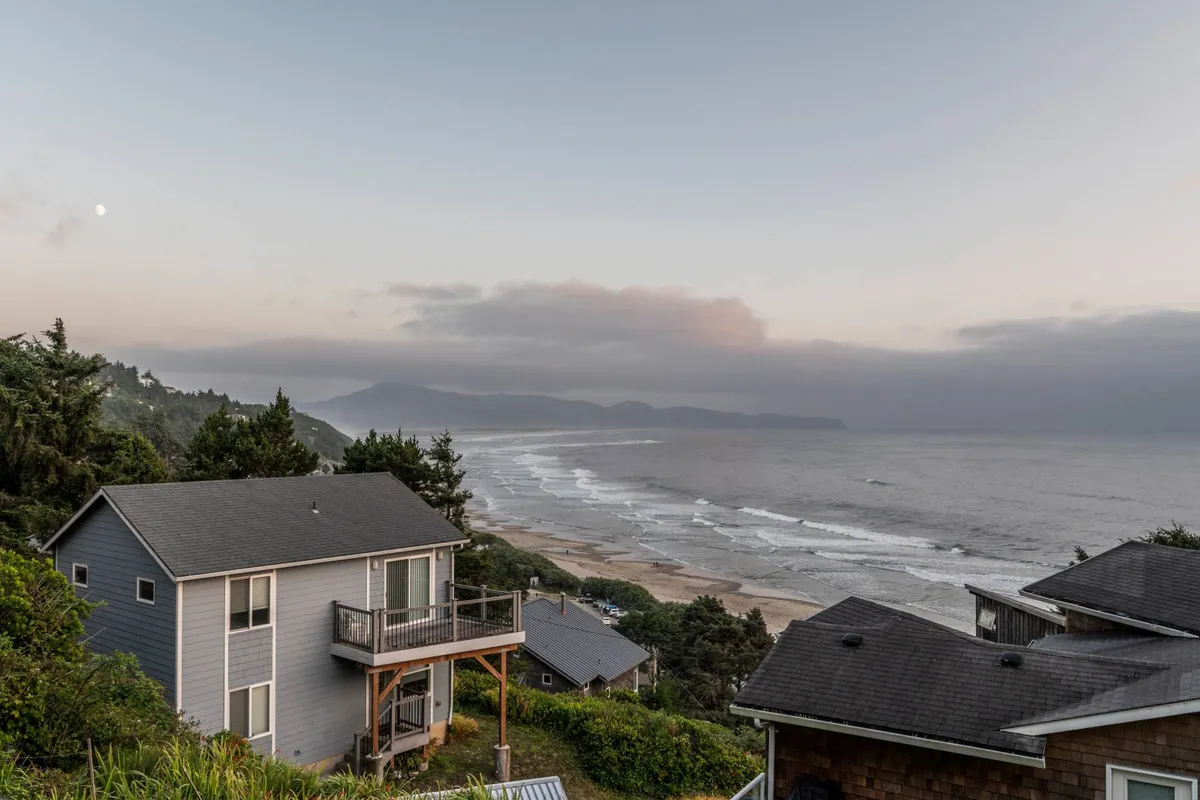 An expansive view of the ocean with distant mountains and the moon visible in the sky, evoking calmness and wonder. The scene invites quiet contemplation and appreciation of nature’s grandeur.