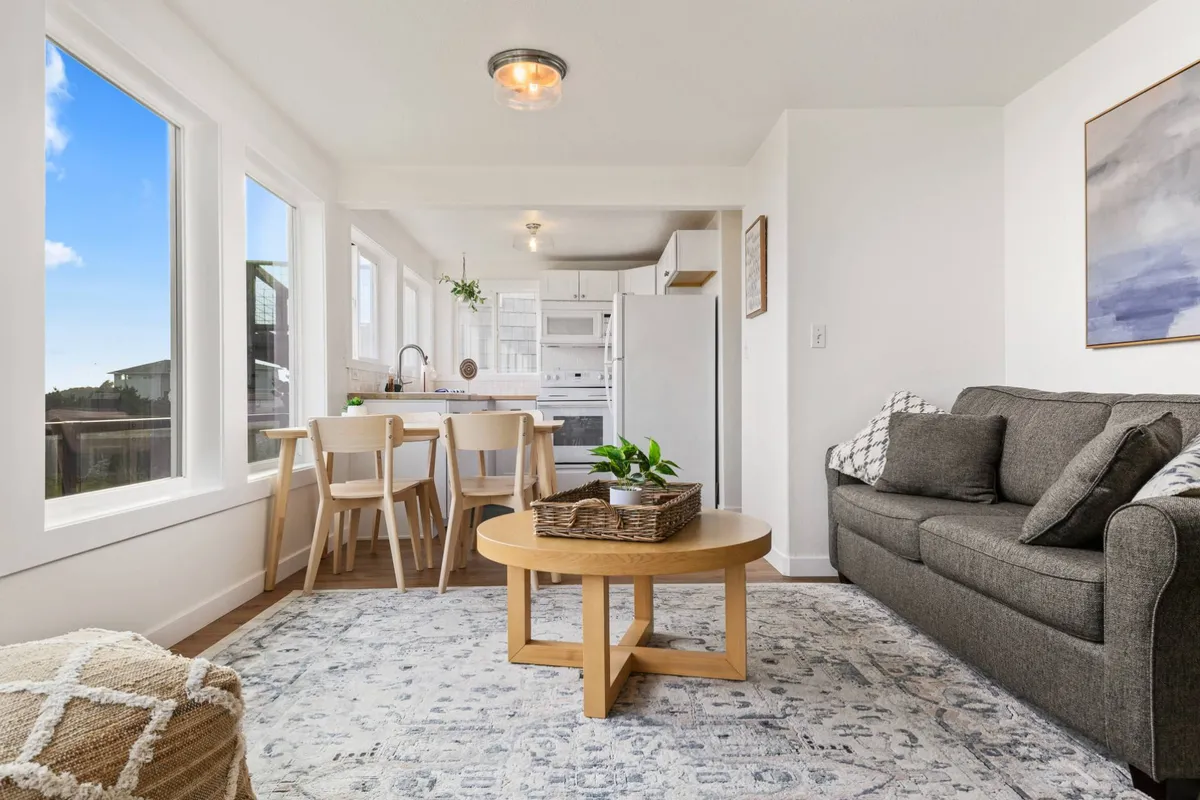 A cozy scene showing a plush sofa and coffee table flowing seamlessly into the dining area and fully equipped kitchen. The entire space features modern décor, warm lighting, and inviting furnishings, illustrating the open-concept design.