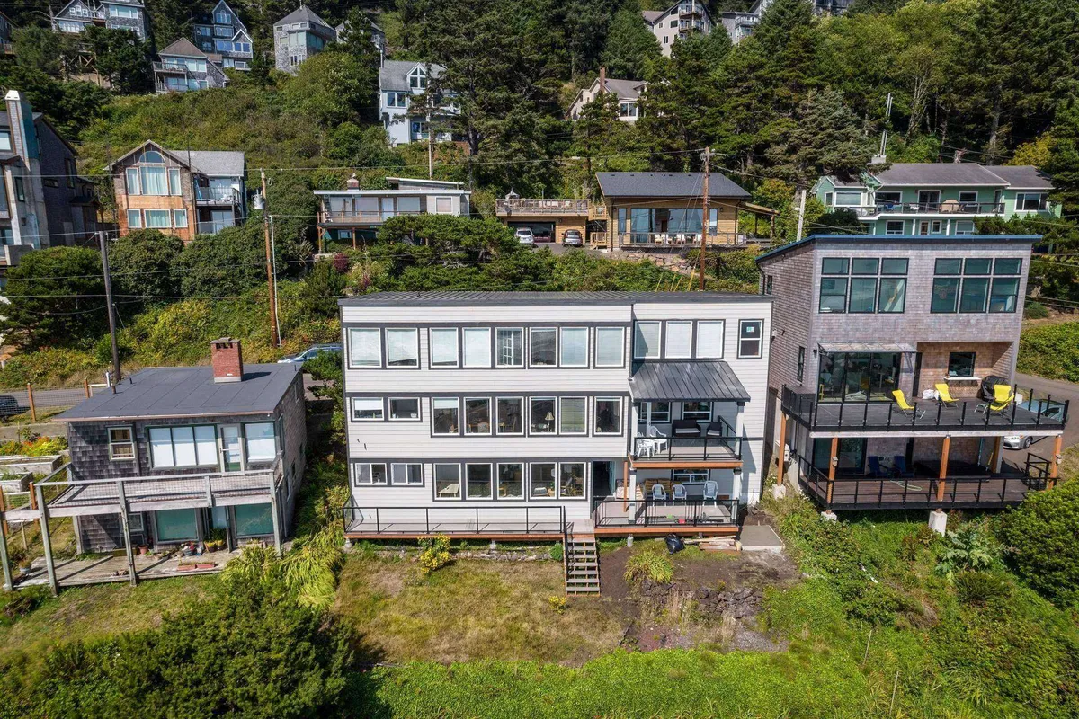 An exterior view of the main house with large windows surrounded by greenery and nearby hillside houses. The porch and natural setting provide a sense of relaxation and connection to the outdoors, ideal after a day of exploring with pets.