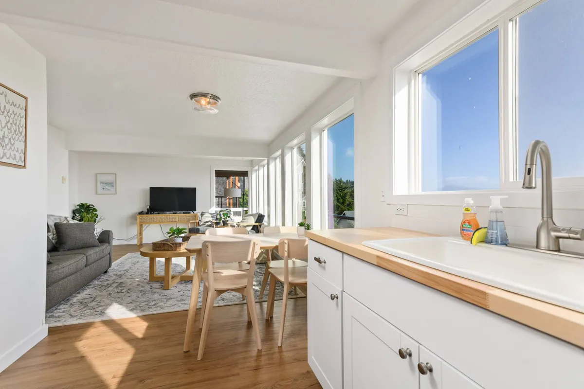 A bright and inviting living/dining area with a large table, comfortable sofa, and expansive windows offering a stunning view of the ocean. Natural light floods the space, creating an uplifting environment ideal for both work and relaxation.